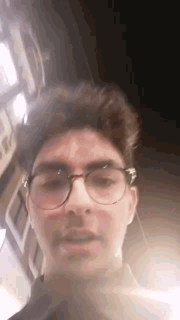 a man wearing glasses and ear buds is standing in front of a building .