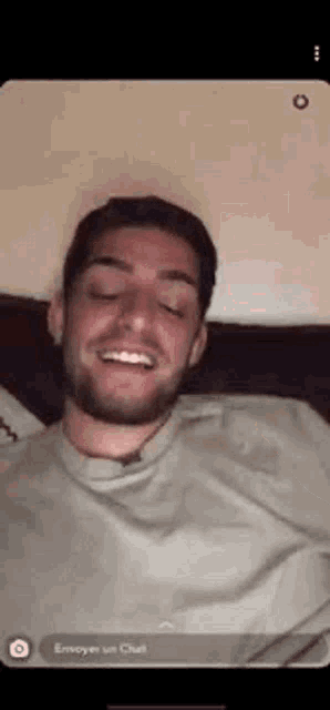 a man with a beard is smiling while laying in bed .