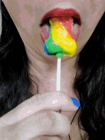 a woman is licking a rainbow colored lollipop in her mouth