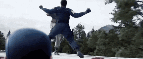 a man in a blue uniform is jumping in the air while another man watches .