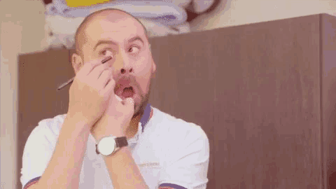 a man wearing a watch is applying makeup to his eye