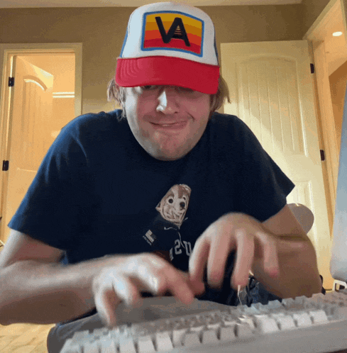 a man wearing a hat with the letter a on it is typing on a keyboard