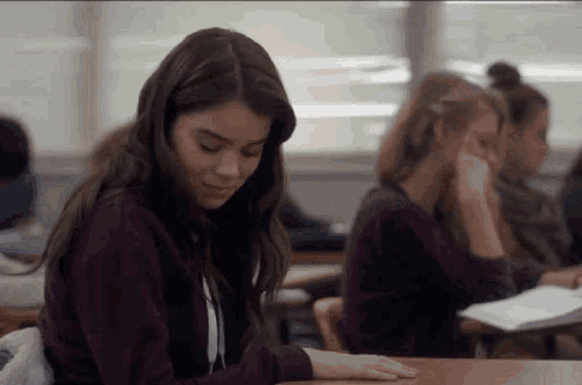 a girl is sitting at a desk in a classroom looking down .