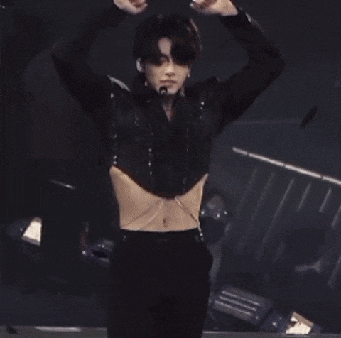 a man in a black crop top is standing on a stage with his hands up .