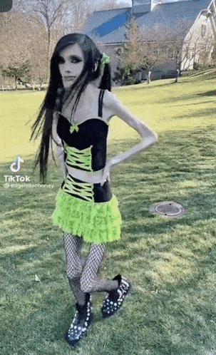 a woman in a green and black dress is standing in the grass .