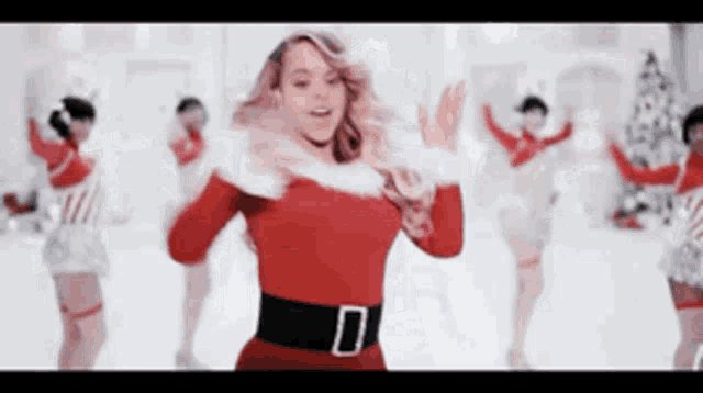a woman in a santa suit is dancing in front of a christmas tree .