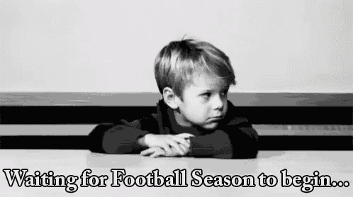 a young boy is sitting at a table waiting for football season to begin .