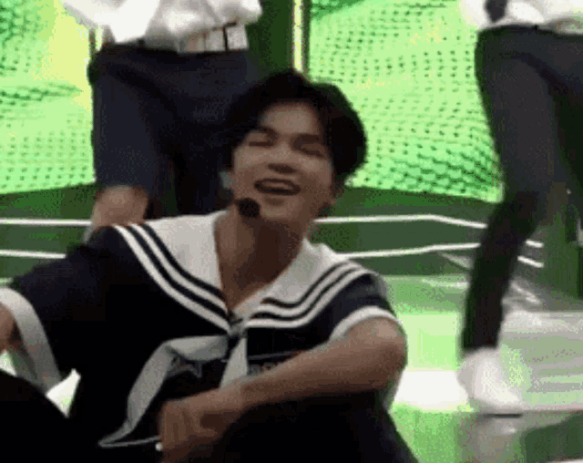 a man in a sailor suit is sitting on the floor and smiling while wearing a microphone .