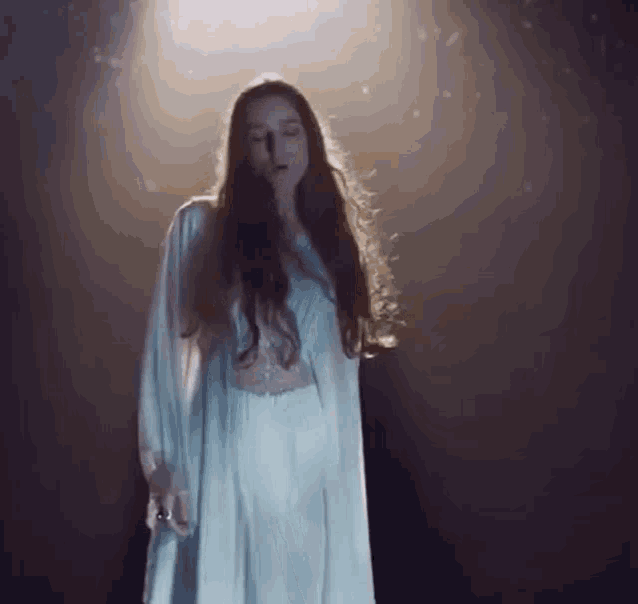a woman in a white dress is standing in a dark room with a light shining on her .