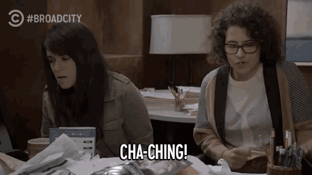two women are sitting at a table and one of them is saying cha-ching