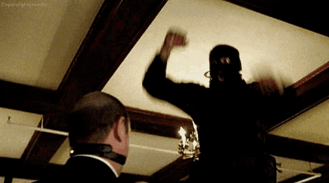 a man in a mask is standing in front of a man in a suit and tie .