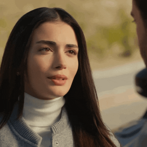 a woman wearing a white turtleneck and a grey jacket looks to the side