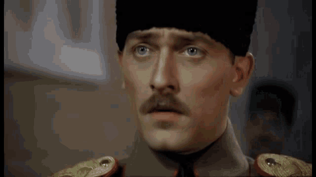 a man with a mustache and a hat is wearing a military uniform and looking at the camera .