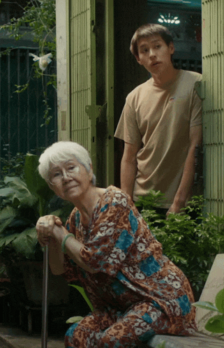 an elderly woman kneeling down with a cane and a young man standing behind her