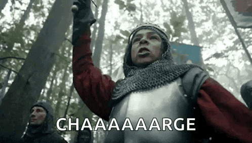 a man in a knight 's armor is standing in the woods holding a sword and shouting .