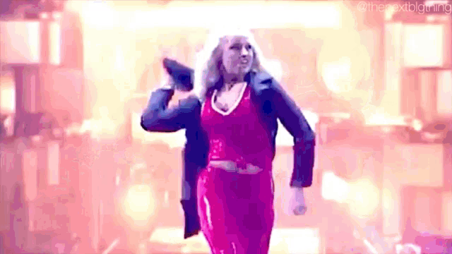 a woman in a red dress and a black jacket is holding a microphone while dancing on a stage .