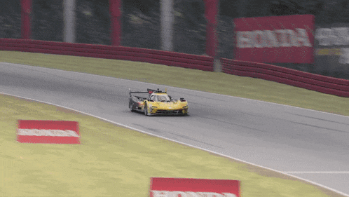 a yellow race car is going down a track with a honda sign in the background