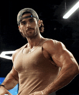 a man with a beard wearing a baseball cap and a tan tank top