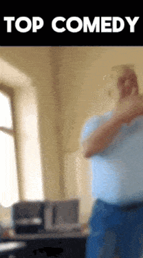 a man in a blue shirt is standing in front of a window with the words top comedy above him
