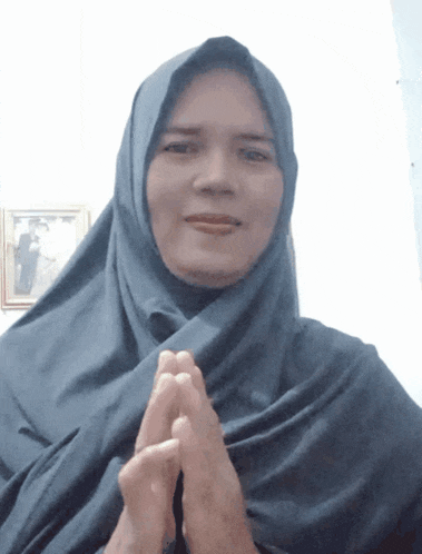 a woman wearing a blue hijab holds her hands together in prayer