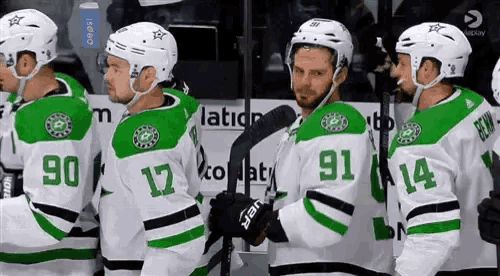 a group of hockey players wearing green and white uniforms are standing next to each other on the ice .