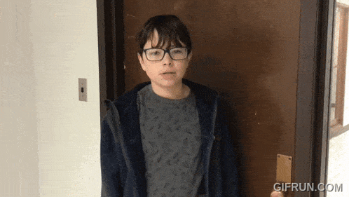 a young boy wearing glasses stands in front of a door with gifrun.com written on the bottom