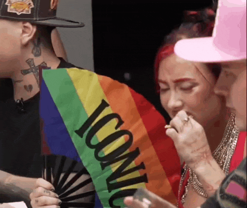 a group of people are sitting around a table holding a fan and a rainbow flag with the word iconic on it .