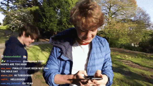 a man in a blue jacket looks at his phone while another man watches