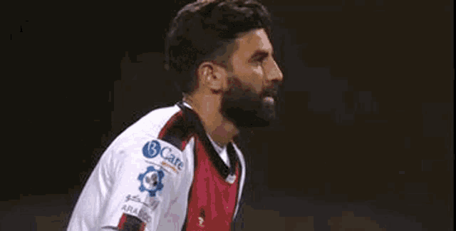 a man with a beard is wearing a white and red soccer jersey on a field .