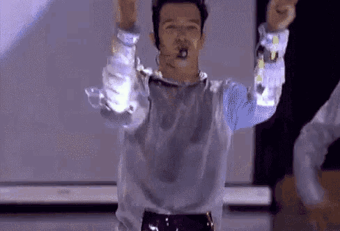 a man is dancing on a stage with his arms in the air and a microphone in his mouth .