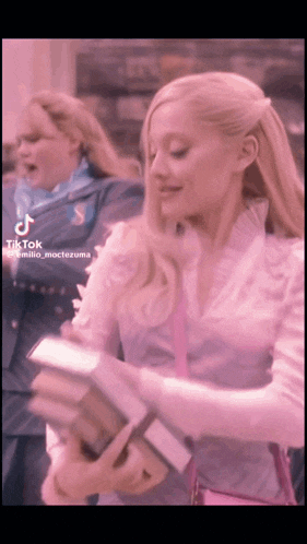 a woman in a pink shirt is holding a book and a tiktok video of her is being shared