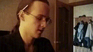 a man wearing glasses is standing in a room with clothes hanging on the wall .