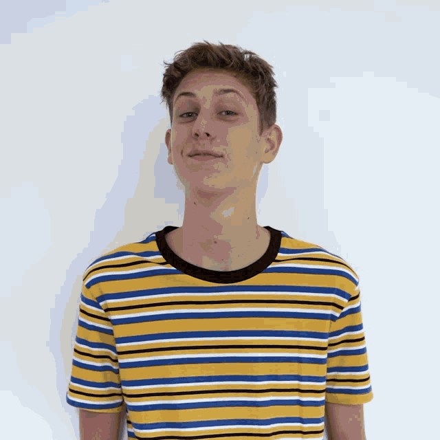 a young man wearing a yellow and blue striped shirt looks at the camera