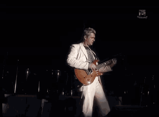 a man in a white suit is playing a guitar in front of a screen that says videocraft