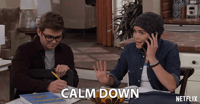 a man and a woman are sitting at a table and the woman is talking on a cell phone and the man is writing