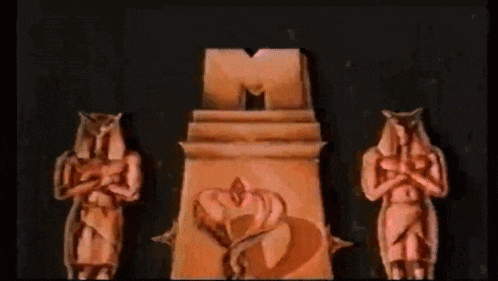 three statues are standing in front of a large m logo