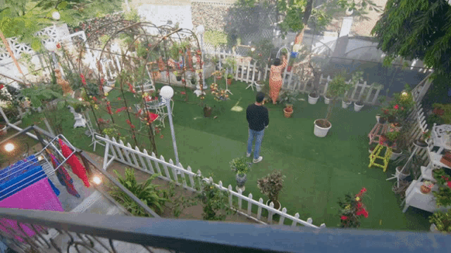 a man in a black jacket stands in a garden surrounded by potted plants and a white picket fence