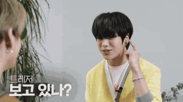 a young man wearing a yellow cardigan is talking to another man