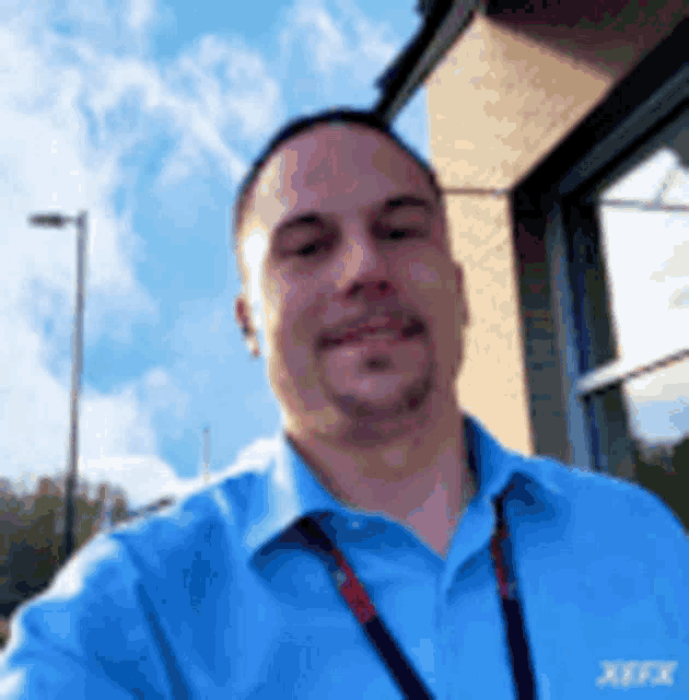 a man in a blue shirt with a lanyard around his neck is taking a selfie