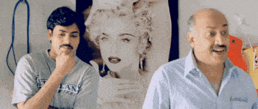 two men are standing in front of a picture of a woman and one of them is wearing a shirt that says ean on it