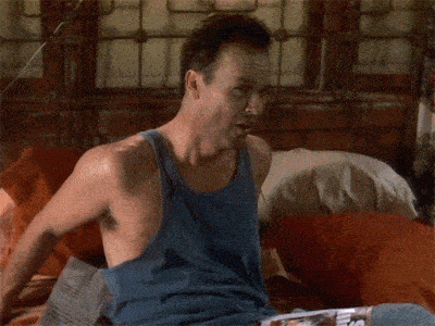 a man in a blue tank top is laying on a bed with a magazine that says ' bar ' on it