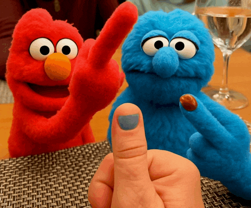 elmo and cookie monster are sitting next to a person 's finger