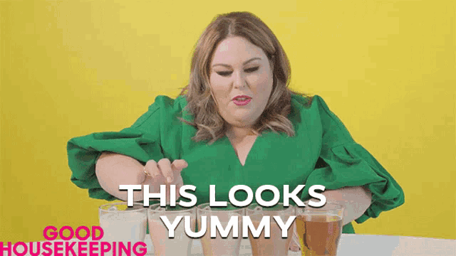 a woman in a green shirt is sitting at a table with glasses of liquid and the words this looks yummy above her