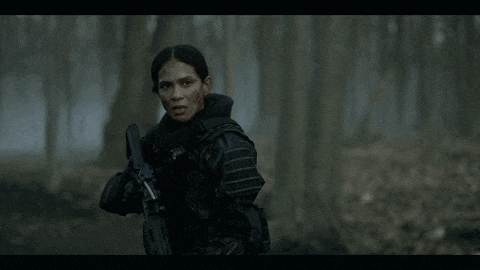 a woman in a military uniform is holding a gun in a dark forest