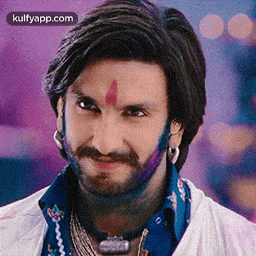 a man with a beard and a red dot on his forehead is smiling with holi paint on his face .