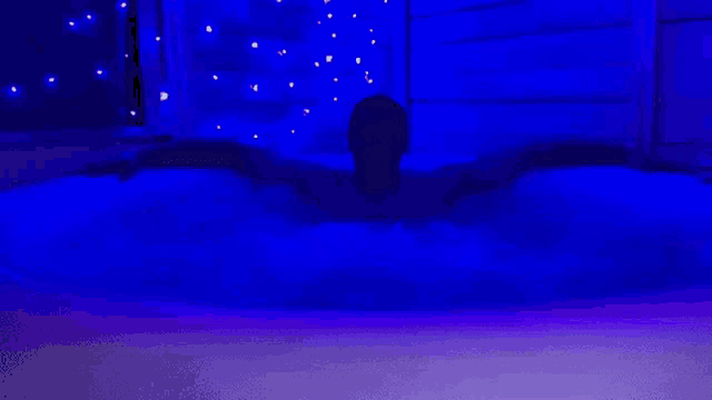a man is laying in a hot tub with blue lights behind him .