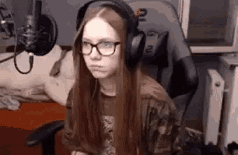 a girl wearing headphones and glasses is sitting in a chair .