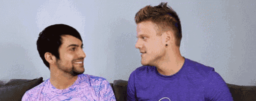 two men are sitting on a couch and smiling at each other .