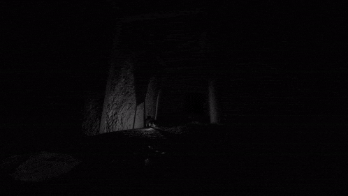 a black and white photo of a dark room with a light coming out of the door .