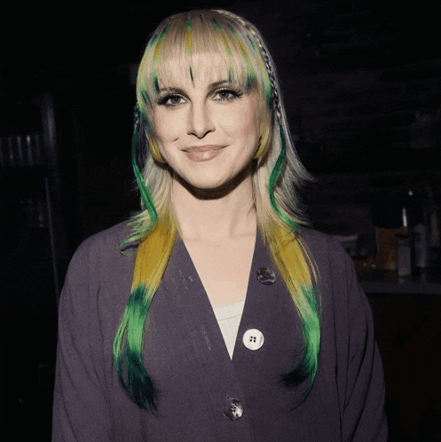a woman with green and yellow hair is wearing a gray jacket with buttons